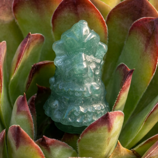 Green crystal Christmas tree carving tucked into a succulent with burgundy-tipped leaves.