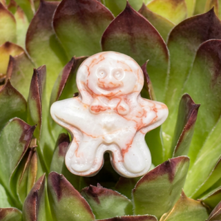 White and red-veined crystal gingerbread man carving displayed among green succulent leaves.