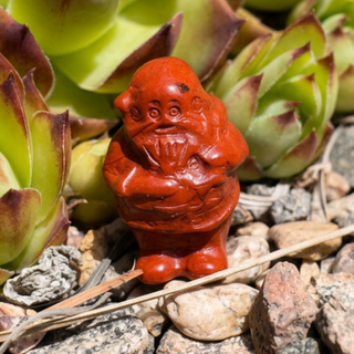 Red crystal Santa carving displayed outdoors among succulents, stones, and natural garden texture.