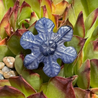 Blue crystal snowflake carving displayed among lush green succulent leaves.