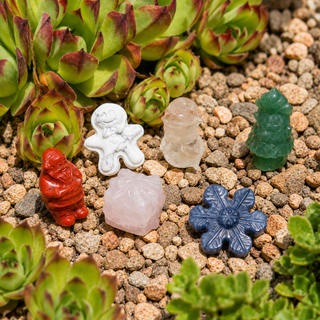 Christmas-themed crystal carvings, including Santa, a gingerbread man, snowman, present, Christmas tree, and snowflake, arranged among succulents and natural stones.