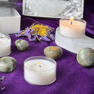 Lit tealight on a selenite stand beside dried blue lotus and labradorite stones on purple velvet
